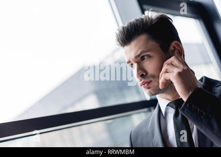 focused handsome bodyguard in suit using earphone Stock Photo
