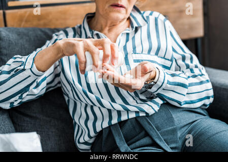 cropped view of sick senior woman sitting on couch and taking pills at home Stock Photo