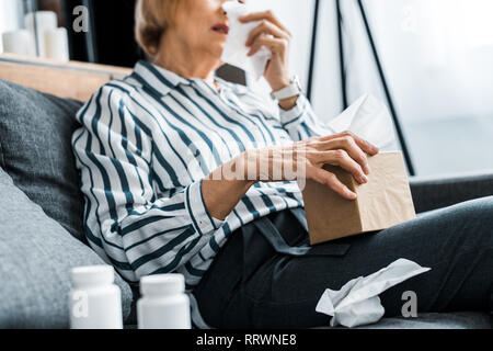 partial view of sick senior woman with runny nose holding tissue box at home Stock Photo