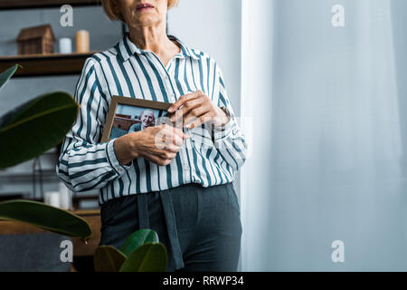 partial view of senior woman holding frame with man on photograph at home with copy space Stock Photo
