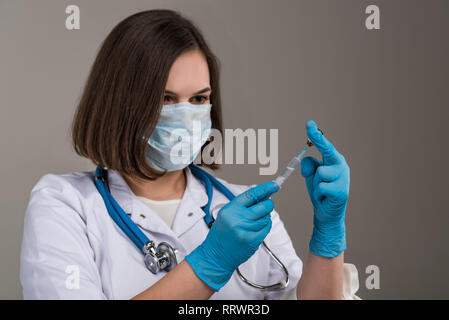 Young attractive nurse with mask fills in syringe in her hand close Stock Photo