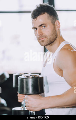 Muscular bodybuilder guy doing exercises with dumbbells in gym - Image Stock Photo