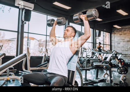 Determined muscular man doing exercises with dumbbells in a gym. - Image Stock Photo