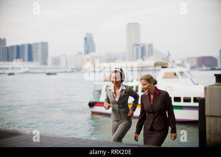 Two smiling businesswomen walking near a waterfront in the city. Stock Photo