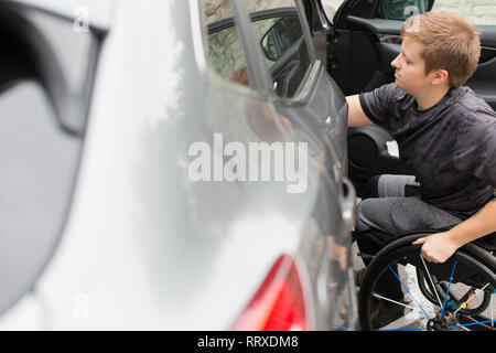 Young woman in wheelchair opening car door Stock Photo