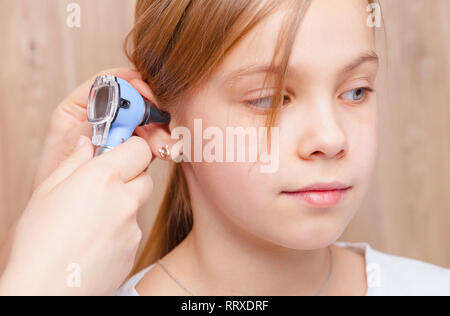 Female pediatrician examines elementary age girl's ear in pediatric clinic. Doctor using a otoscope or auriscope to check ear canal and eardrum membra Stock Photo