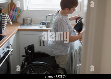 Young woman with wheelchair pouring tea in apartment kitchen Stock Photo
