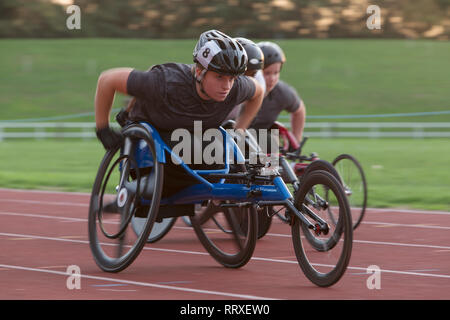 Determined young female paraplegic athlete speeding along sports track in wheelchair race Stock Photo