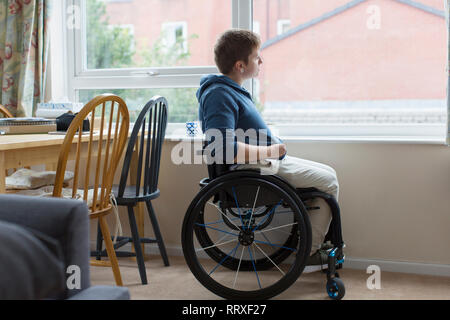 Thoughtful young woman in wheelchair looking out window Stock Photo