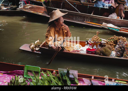 Asian senior adult Woman smoking cigarette and sailing on boat with goods Stock Photo
