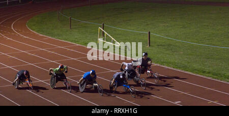 Paraplegic athletes speeding along sports track in wheelchair race at night Stock Photo