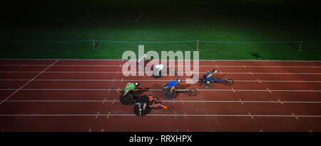 Paraplegic athletes racing along sports track in wheelchair race in night Stock Photo