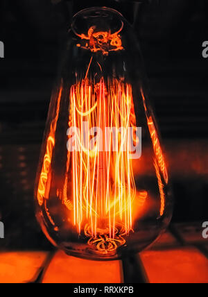 Bright glowing clear glass lamp pear shaped close up. Illumination edison retro lamp dark background. Antique vintage filament light bulb. Stock Photo