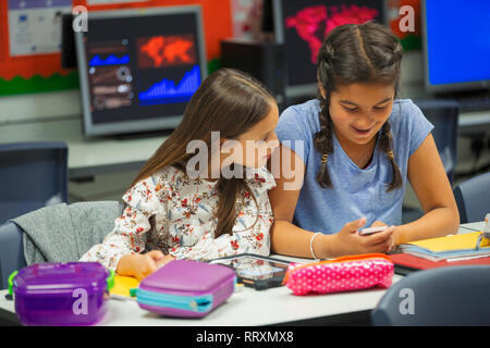 Junior high school girl students using smart phone at desk in classroom Stock Photo