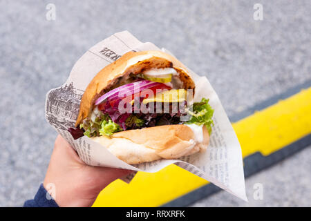 Hand of a young man holding an organic vegan burger with seitan patty in his hand during a street food festival Stock Photo