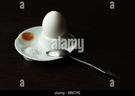 boiled egg with spoon, stand and salt on dark background Stock Photo
