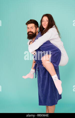 Handsome young man piggybacking beautiful woman. Couple in bathrobes having fun turquoise background. Lets stay at home and have fun. They always have fun together. Enjoying every second together. Stock Photo