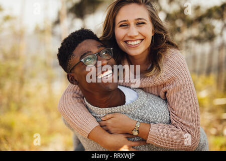 Young african man piggybacking his girlfriend. Interracial couple having fun outdoors. Stock Photo