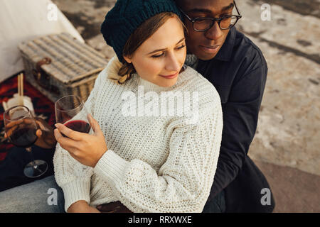 Loving couple on picnic sitting together and looking away. Man sitting behind woman and hugging her. Stock Photo