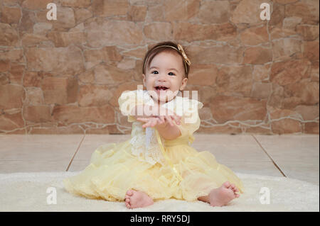 One baby girl in yellow dress smiling and clapping Stock Photo