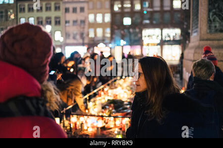 STRASBOURG, FRANCE - DEC 13, 2018: Sad young woman mourning gathering near General Kleber statue to attend a vigil with multiple light candles flowers and messages for the victims of terrorist Cherif Chekatt at Christmas Market Stock Photo