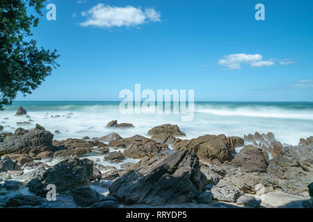 Waves smoothed by long exposure washing in around rocky foreshore at base of Mount Maunganui, Tauranga New Zealand Stock Photo