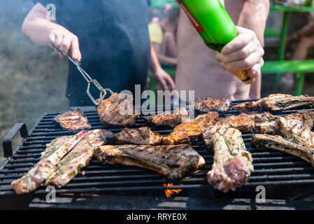 Friends frying the meat ribs and steaks, barbecue on open air, picnic, rest on weekends Stock Photo