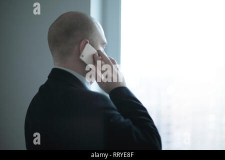 rear view .businessman with smartphone looking out the window of the office. Stock Photo