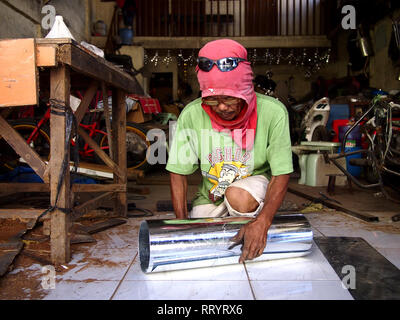 ANTIPOLO CITY, PHILIPPINES - FEBRUARY 21, 2019: A carpenter wearing a shirt on his head as protective gear works inside his workshop. Stock Photo