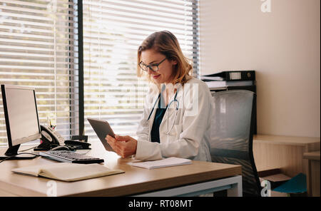 Female doctor using a digital tablet at her desk in the clinic. Female doctor working on her tablet pc in her office. Stock Photo