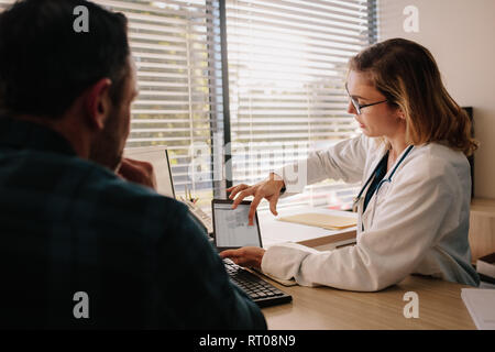 Female doctor holding digital tablet, showing test results to patient in hospital. Doctor and patient having medical consultation over test results in Stock Photo