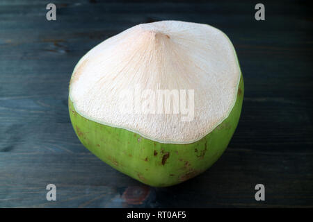 One fresh young coconut ready to be opened for juice isolated on dark colored wooden table Stock Photo