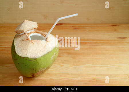 Fresh young coconut with white straw isolated on light brown wooden table Stock Photo