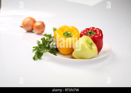 Three delicious ripe Bulgarian peppers, lime, red, orange, and two onions on a plate, on a white background, side view Stock Photo