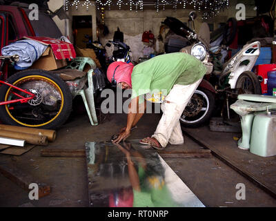 ANTIPOLO CITY, PHILIPPINES - FEBRUARY 21, 2019: A carpenter wearing a shirt on his head as protective gear works inside his workshop. Stock Photo