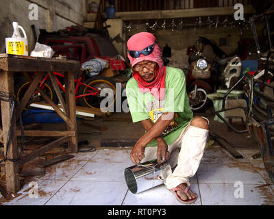 ANTIPOLO CITY, PHILIPPINES - FEBRUARY 21, 2019: A carpenter wearing a shirt on his head as protective gear works inside his workshop. Stock Photo