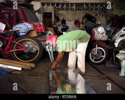 ANTIPOLO CITY, PHILIPPINES - FEBRUARY 21, 2019: A carpenter wearing a shirt on his head as protective gear works inside his workshop. Stock Photo