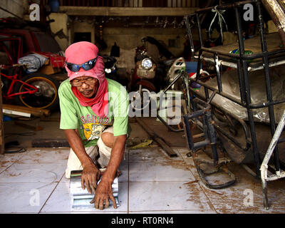 ANTIPOLO CITY, PHILIPPINES - FEBRUARY 21, 2019: A carpenter wearing a shirt on his head as protective gear works inside his workshop. Stock Photo