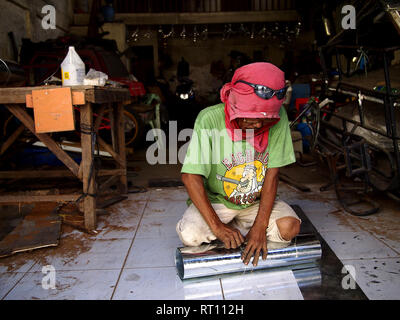 ANTIPOLO CITY, PHILIPPINES - FEBRUARY 21, 2019: A carpenter wearing a shirt on his head as protective gear works inside his workshop. Stock Photo