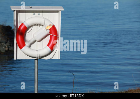 Red white lifebuoy with ropes hanging in wooden box on a lake coast Stock Photo