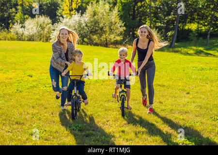 Two happy mothers teach their happy sons to ride a bike Stock Photo