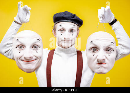 Portrait of a pantoomime holding two facial masks with different emotions on the yellow background. Concept of personality split Stock Photo