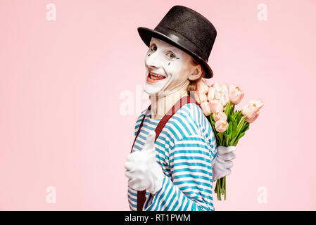 Emotional pantomime posing with tulip bouquet on the pink background indoors. Valentine's Day and love concept Stock Photo