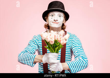 Emotional pantomime posing with tulip bouquet on the pink background indoors. Valentine's Day and love concept Stock Photo