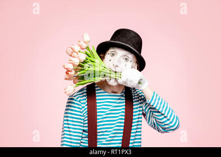 Emotional pantomime posing with tulip bouquet on the pink background indoors. Valentine's Day and love concept Stock Photo