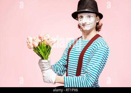 Emotional pantomime posing with tulip bouquet on the pink background indoors. Valentine's Day and love concept Stock Photo