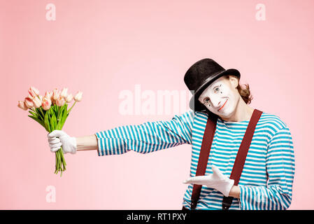 Emotional pantomime posing with tulip bouquet on the pink background indoors. Valentine's Day and love concept Stock Photo