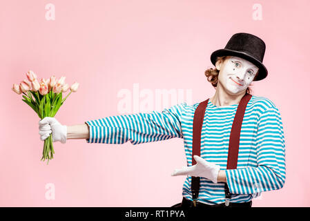 Emotional pantomime posing with tulip bouquet on the pink background indoors. Valentine's Day and love concept Stock Photo