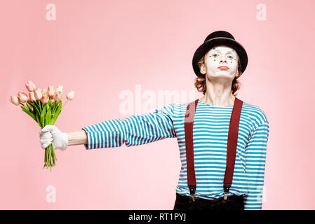 Emotional pantomime posing with tulip bouquet on the pink background indoors. Valentine's Day and love concept Stock Photo