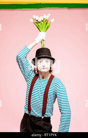 Emotional pantomime posing with tulip bouquet on the pink background indoors. Valentine's Day and love concept Stock Photo